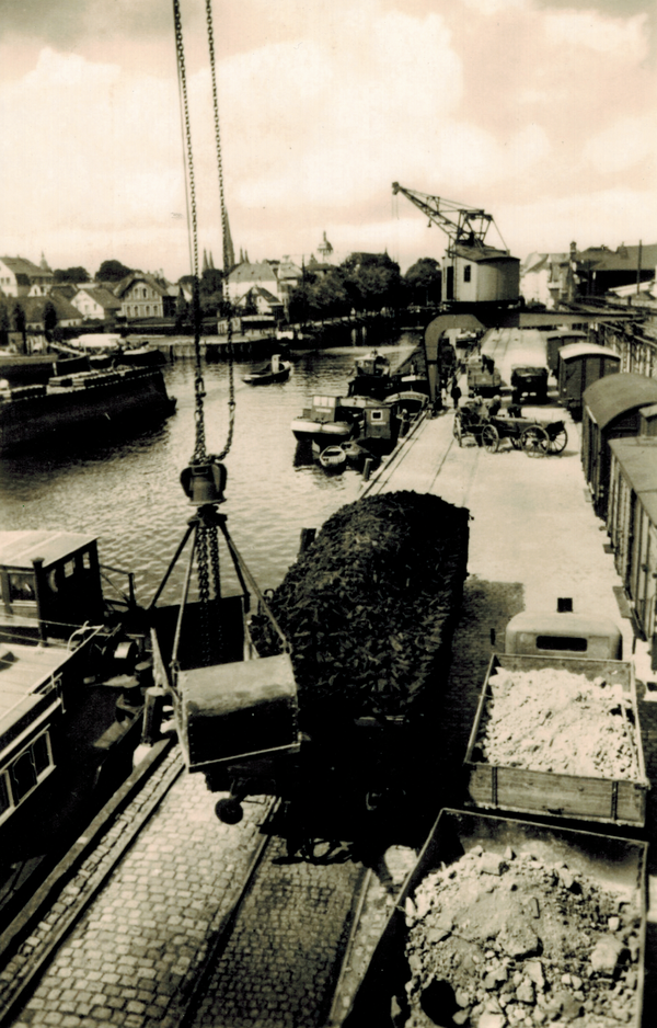 Mehrere Kräne waren am Stadthafen im Einsatz, darunter auch Halbportalkräne. Diese laufen über eine Schiene am Boden und eine Schiene an einer Mauer oder Brücke, 1950er Jahre, Foto: Stadtmuseum Oldenburg