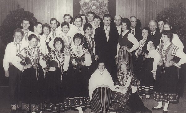 Lettische Kolonie Rennplatzsiedlung: Chor in traditioneller Tracht vor lettischem Wappen, 1950er Jahre. Foto: Hermann Sokolowsky/Stadtmuseum Oldenburg.