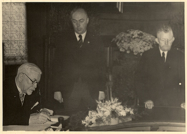 Johann Schütte trägt sich 1938 unter Augen von Oberbürgermeister und NSDAP-Mitglied Dr. Heinrich Karl Paul Rabeling in das Goldene Buch ein. Bild: Stadtmuseum Oldenburg.